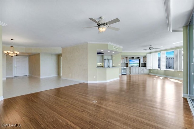 unfurnished living room with baseboards, wood finished floors, crown molding, and ceiling fan with notable chandelier