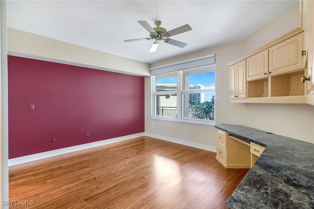 interior space featuring ceiling fan, built in study area, baseboards, and wood finished floors