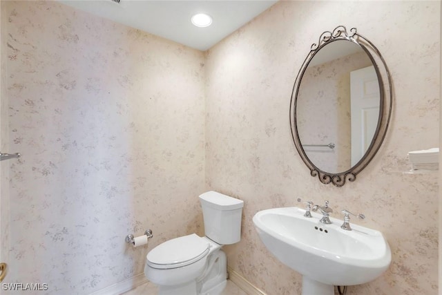 half bath with wallpapered walls, toilet, baseboards, and a sink