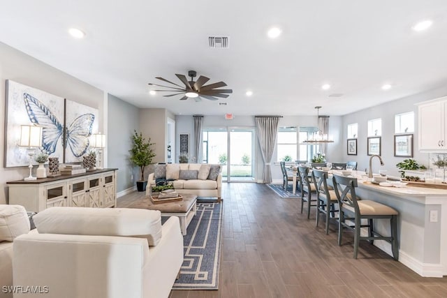 living area with ceiling fan with notable chandelier, visible vents, dark wood-type flooring, and recessed lighting