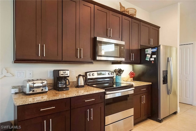 kitchen with appliances with stainless steel finishes, light tile patterned flooring, light stone counters, and dark brown cabinets