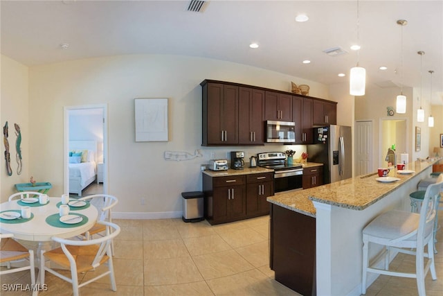 kitchen featuring dark brown cabinetry, light stone counters, a breakfast bar, stainless steel appliances, and a sink