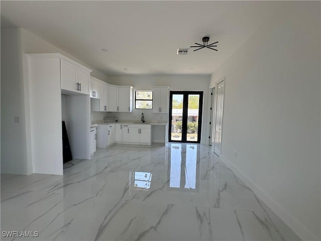 kitchen featuring a sink, visible vents, white cabinets, baseboards, and marble finish floor