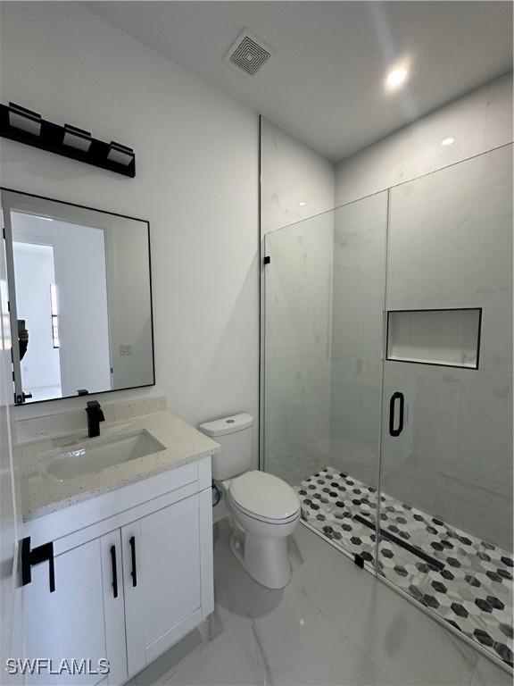 bathroom featuring toilet, vanity, visible vents, marble finish floor, and a stall shower