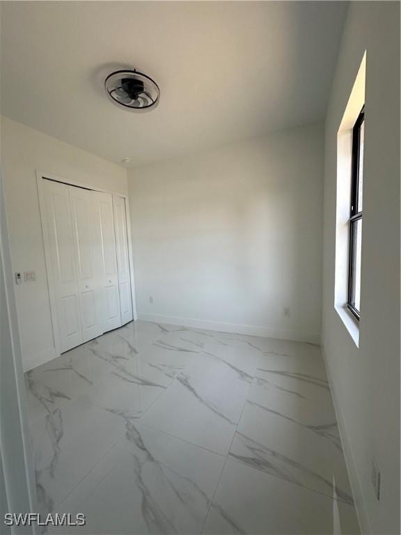 unfurnished bedroom with marble finish floor, a closet, and baseboards