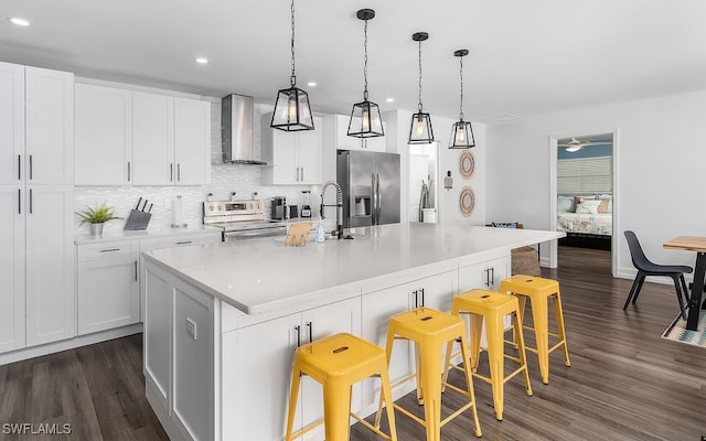 kitchen featuring dark wood-style floors, wall chimney exhaust hood, stainless steel appliances, and backsplash