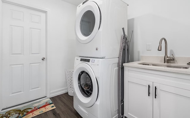 laundry room featuring dark wood-style flooring, cabinet space, a sink, stacked washing maching and dryer, and baseboards