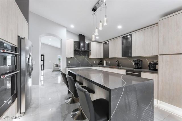 kitchen featuring a breakfast bar, arched walkways, wall chimney exhaust hood, modern cabinets, and stainless steel fridge with ice dispenser