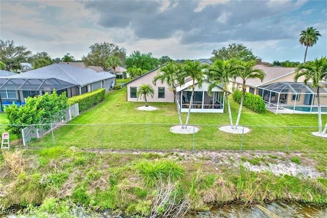 rear view of house featuring glass enclosure, a fenced backyard, and a yard