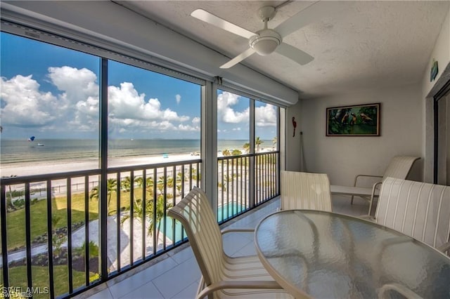 sunroom / solarium with a ceiling fan, a water view, and a beach view