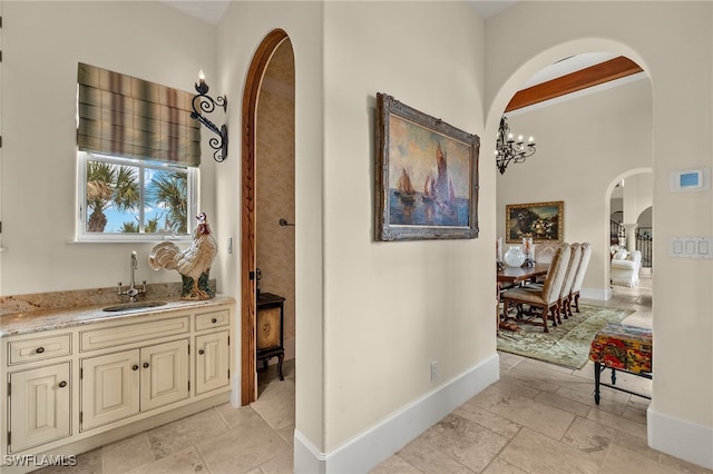 corridor featuring arched walkways, baseboards, a sink, and stone tile floors