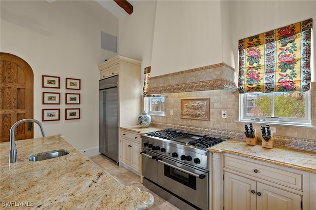 kitchen with light stone counters, a sink, visible vents, high quality appliances, and cream cabinetry