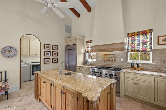 kitchen with light stone counters, washing machine and dryer, a sink, cream cabinetry, and high end appliances