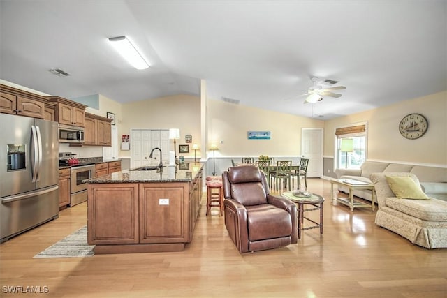 kitchen featuring stainless steel appliances, open floor plan, a sink, and dark stone countertops