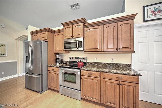 kitchen featuring brown cabinets, light wood finished floors, stainless steel appliances, visible vents, and dark stone countertops