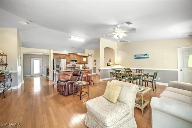 living area featuring light wood-type flooring, arched walkways, visible vents, and vaulted ceiling