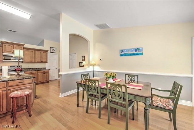 dining space featuring baseboards, visible vents, vaulted ceiling, and light wood finished floors