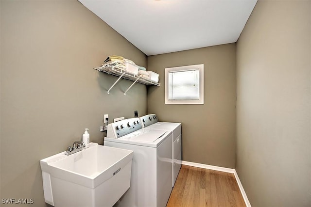 washroom with laundry area, baseboards, washer and dryer, light wood-type flooring, and a sink