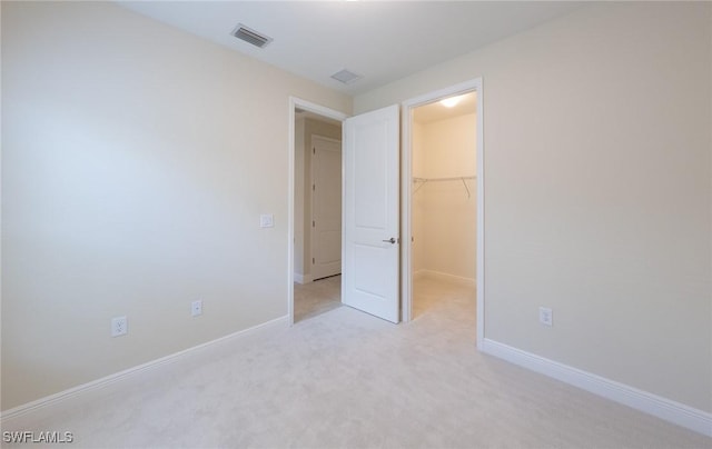 unfurnished bedroom with baseboards, visible vents, light colored carpet, a walk in closet, and a closet