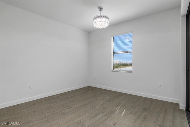 unfurnished room with a chandelier, wood finished floors, and baseboards