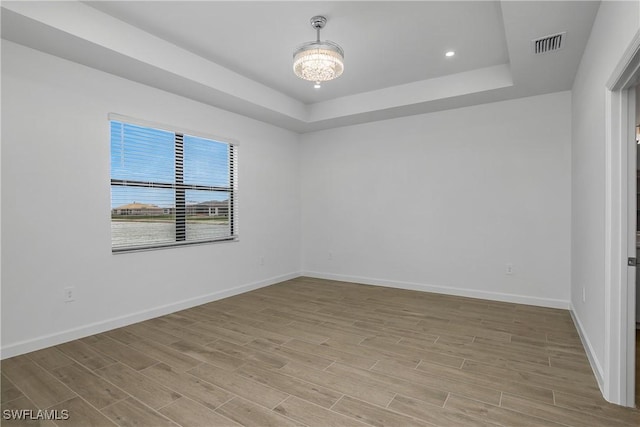 unfurnished room with light wood-style floors, baseboards, visible vents, and a tray ceiling