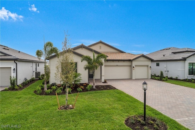 ranch-style home with decorative driveway, an attached garage, central AC unit, a front yard, and a tiled roof