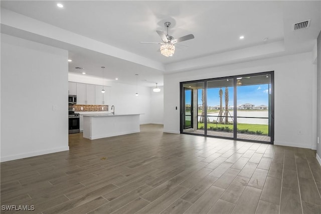 unfurnished living room featuring a raised ceiling, visible vents, a sink, wood finished floors, and baseboards