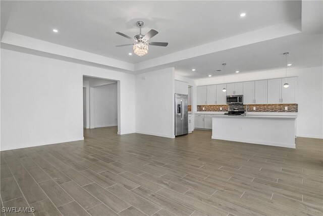 kitchen featuring appliances with stainless steel finishes, open floor plan, wood finished floors, a tray ceiling, and backsplash