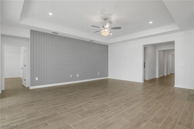 empty room featuring ceiling fan, a tray ceiling, wood finish floors, and visible vents