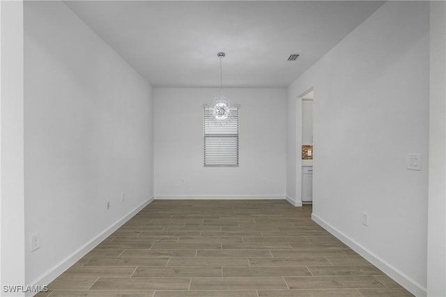 unfurnished dining area featuring an inviting chandelier, wood finished floors, visible vents, and baseboards