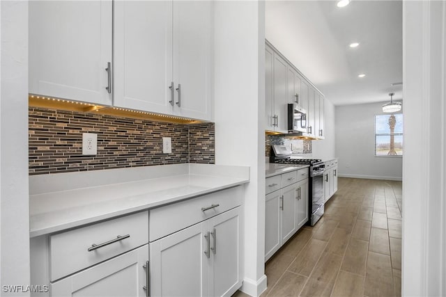 kitchen featuring light wood-style floors, light countertops, decorative backsplash, stainless steel microwave, and gas range