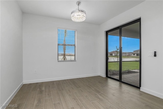 empty room with baseboards, wood finished floors, and a notable chandelier