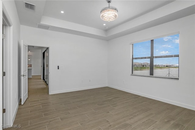 empty room featuring an inviting chandelier, baseboards, a raised ceiling, and wood finished floors