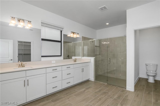 bathroom featuring double vanity, a shower stall, wood tiled floor, and a sink