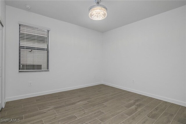 empty room with baseboards, a chandelier, and wood tiled floor