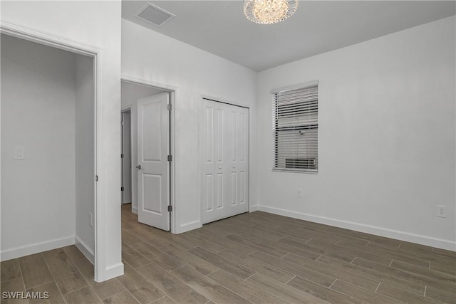 unfurnished bedroom featuring a notable chandelier, wood finished floors, visible vents, baseboards, and a closet