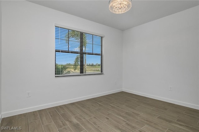 unfurnished room featuring wood tiled floor, baseboards, and a notable chandelier