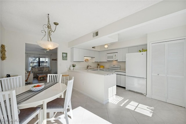 kitchen featuring white appliances, visible vents, a peninsula, light countertops, and a sink