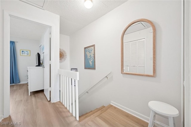 corridor featuring light wood-style flooring, baseboards, a textured ceiling, and an upstairs landing