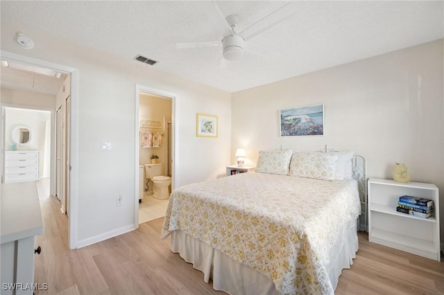 bedroom with a textured ceiling, connected bathroom, light wood-style flooring, visible vents, and attic access