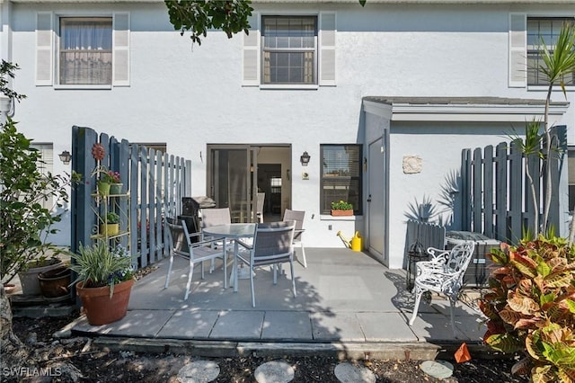 rear view of property with a patio area, fence, outdoor dining area, and stucco siding