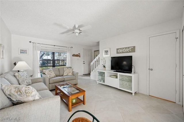 living room with a textured ceiling, ceiling fan, light tile patterned floors, and stairway