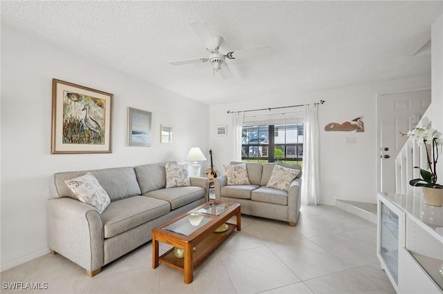 living area featuring light tile patterned floors, ceiling fan, baseboards, and a textured ceiling