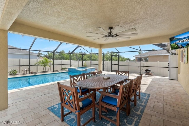 view of swimming pool with a patio, a pool with connected hot tub, glass enclosure, fence, and ceiling fan