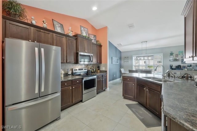 kitchen with stainless steel appliances, a sink, vaulted ceiling, dark brown cabinets, and dark countertops