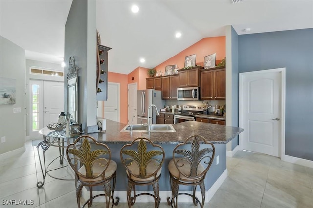 kitchen with light tile patterned floors, stainless steel appliances, a peninsula, a sink, and a kitchen breakfast bar