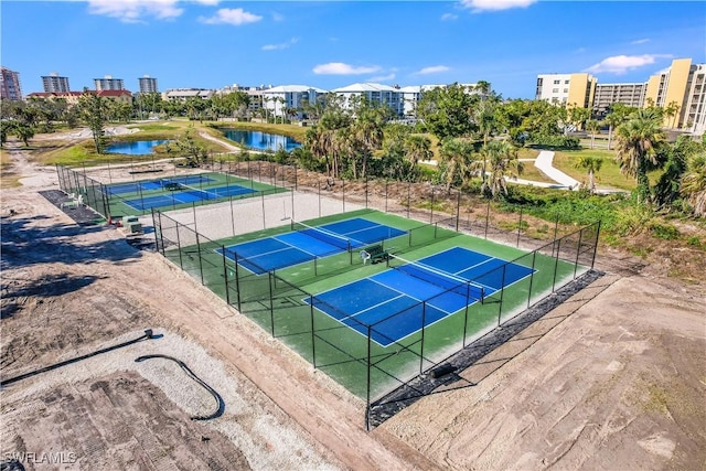 view of tennis court featuring a water view, fence, and a city view