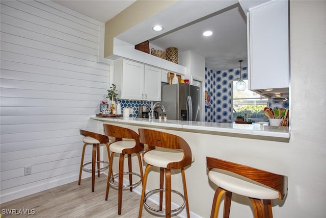 kitchen featuring white cabinets, stainless steel fridge with ice dispenser, light countertops, light wood-style floors, and a sink