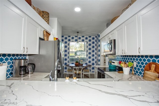 kitchen featuring white cabinets, pendant lighting, stainless steel appliances, and light stone counters