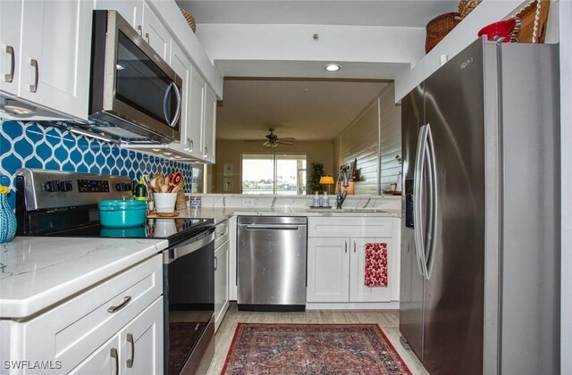 kitchen featuring white cabinets, ceiling fan, light stone counters, appliances with stainless steel finishes, and a sink